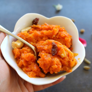carrot halwa served in ahwite bowl with spoon and topped with cashew and raisins