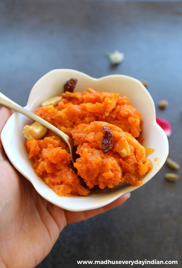 carrot halwa served in ahwite bowl with spoon and topped with cashew and raisins