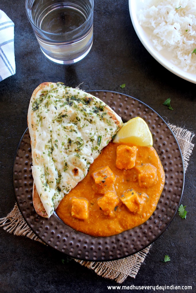 paneer butter masala served in a white bowl with naan, water  and rice