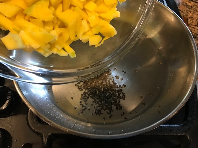 mango being added to the hot oil and mustard