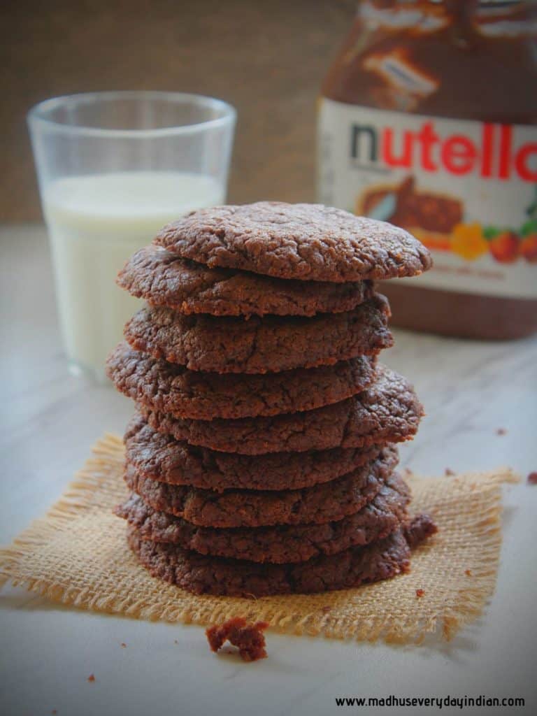 stacked nutella cookies served with cup of milk and nutella bottle in the back ground