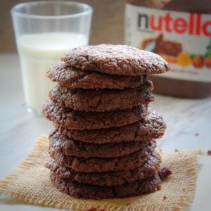stacked nutella cookies served with cup of milk and nutella bottle in the back ground