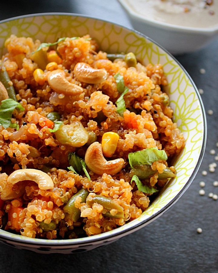 quinoa upma served in abowl topped with cashew and coriander and peanut chutney on the side.