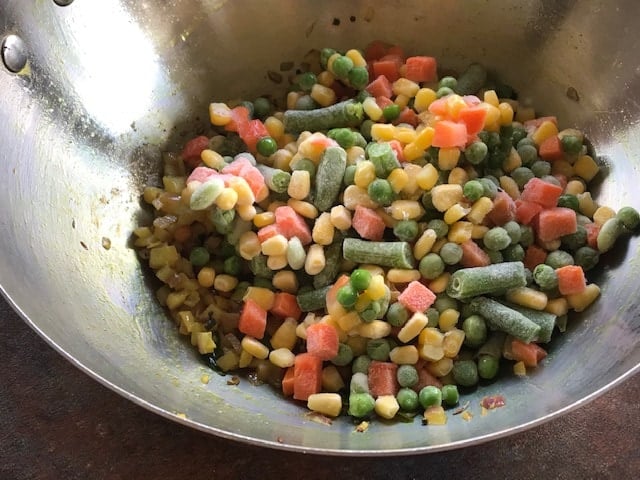 frozen veggies added to the wok whoch has sauteed onion and tempering of mustard and cumin seeds