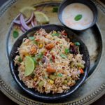vegetale pulao served in a black bowl and served with onion, lime and yogurt