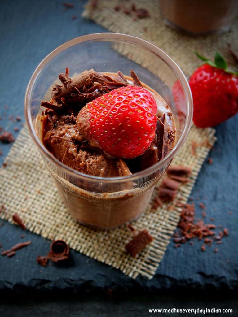 nutella mousse served in a small glass cup with chocolate shaving, strawberry and a spoon on the side.