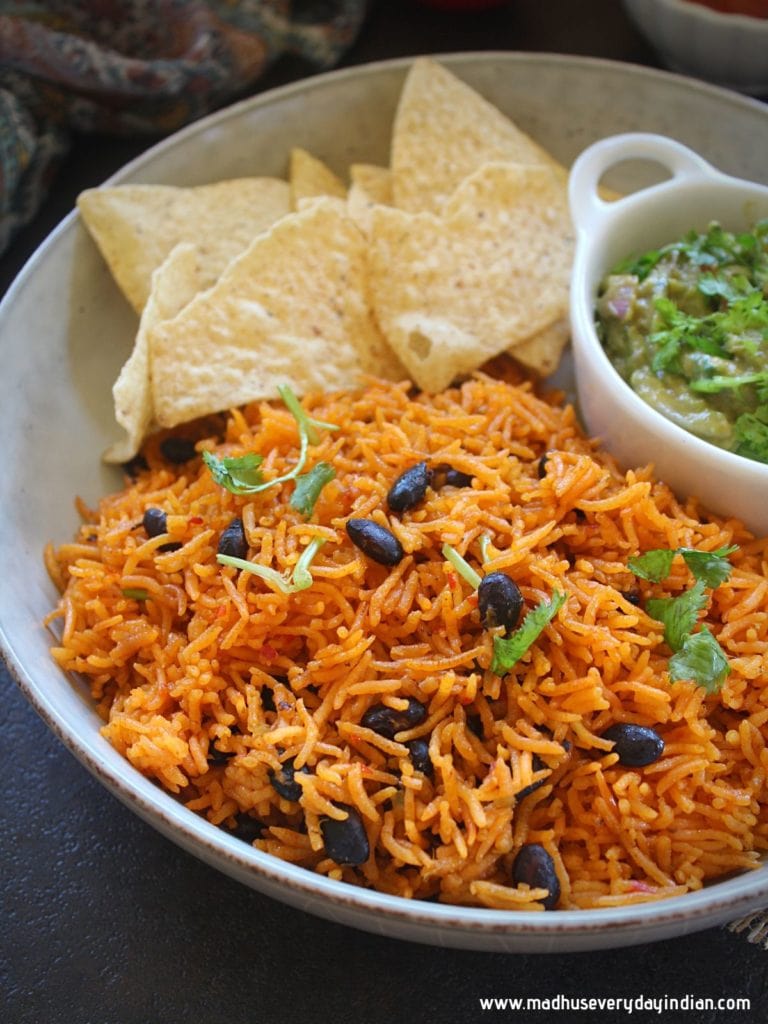 puerto rican yellow rice served in a white plate with chips and guacamole