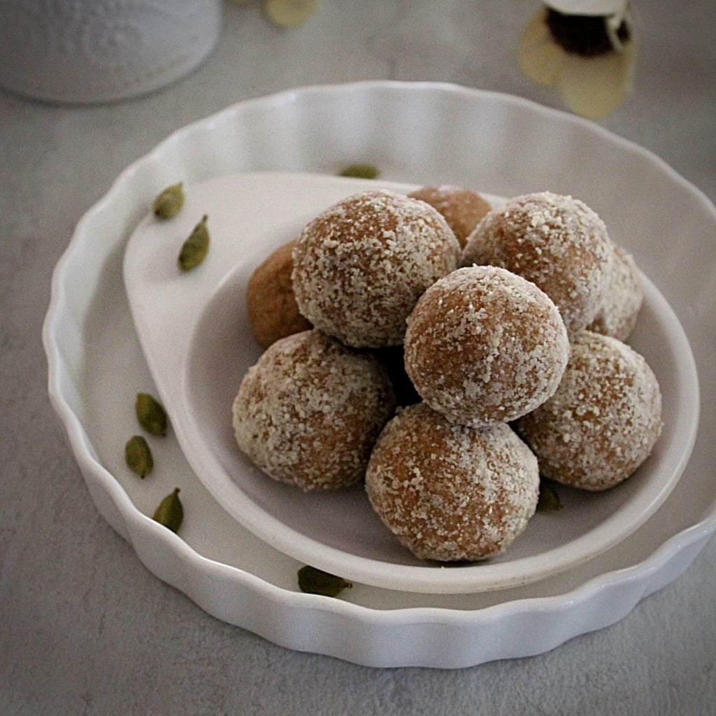 almond ladoo made with almond flour arranged in a double white place and garnished with cardamom.