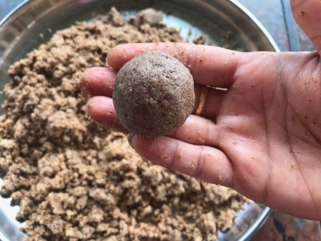 flax seed ladoo being held in  the hand and the powdered mixture in a plate