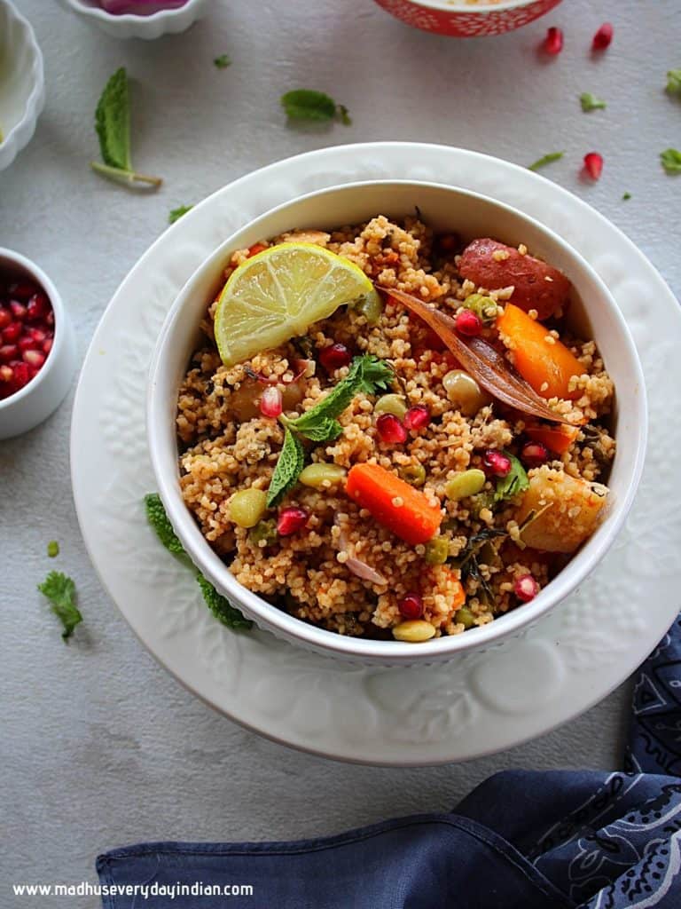 millet pulao served in a white bowl with lemon wedge, onion, pomegranate