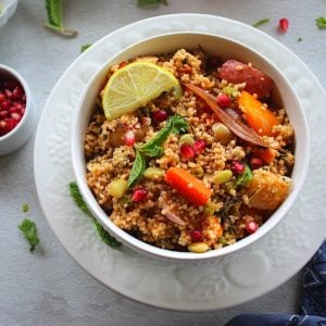 millet pulao served in a white bowl with lemon wedge, onion, pomegranate