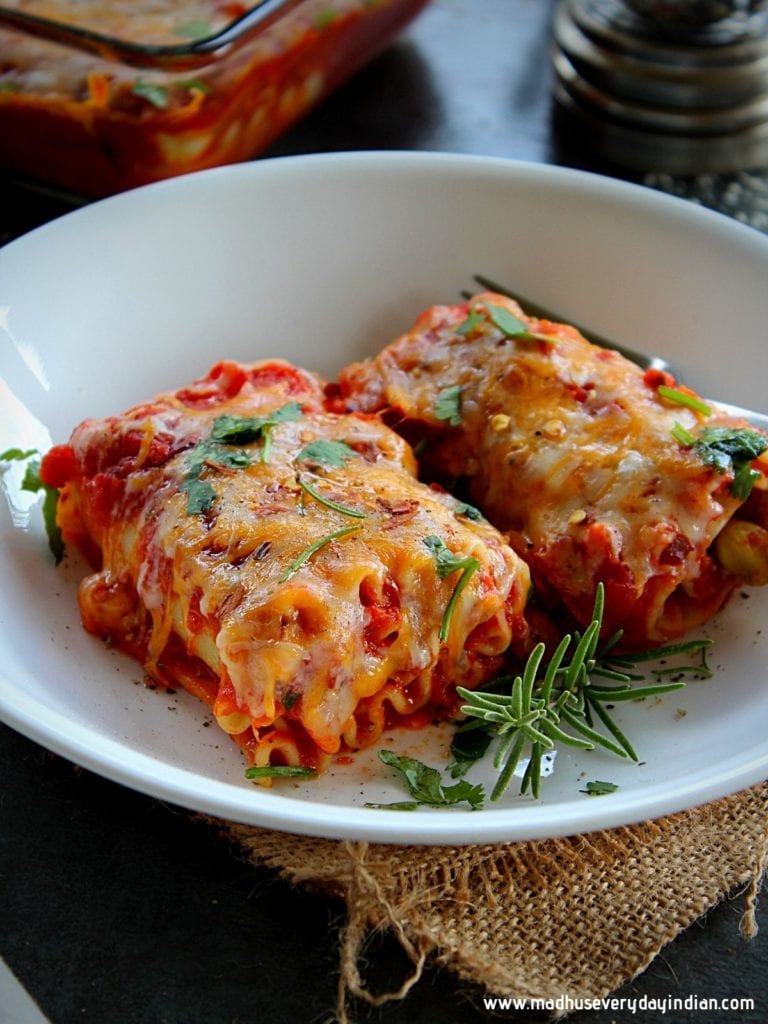 2 veggie lasagna rolls ups served in a white plate garnished with fresh herbs