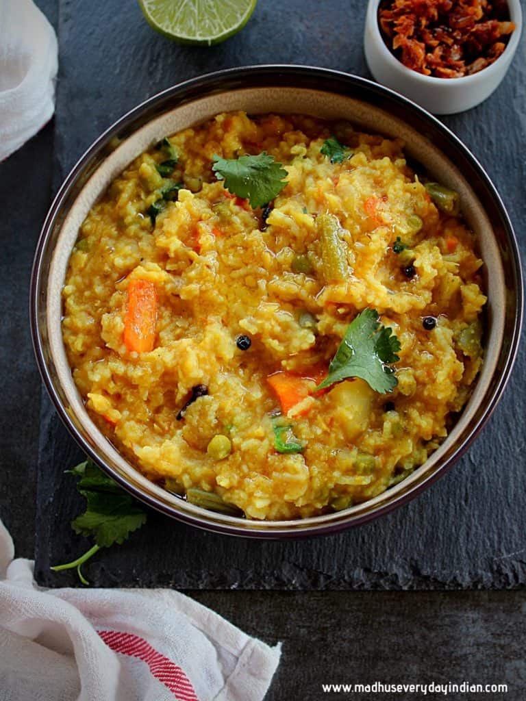 khichdi served in a brown bowl and on the side are garlic pickle and lemon 