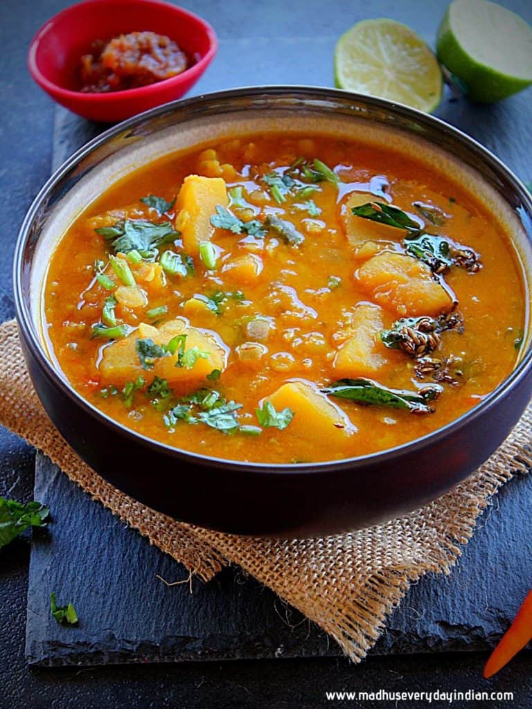 pumpkin dal served in a brown bowl garmished with cilantro and atempering of mustard, cumin and curry leaves.