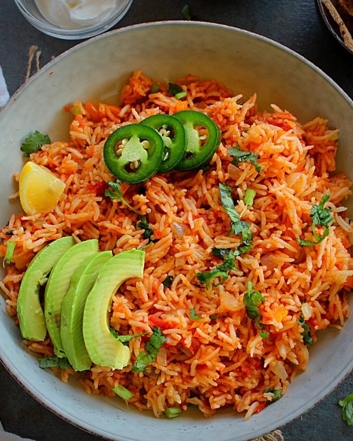 spanish rice served in a white plate with guacamole and jalapeno