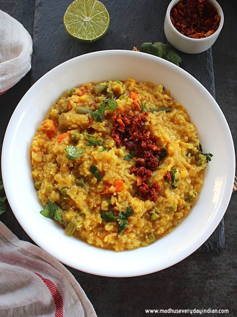 khichdi served in a white place with garlic pickle and garnished with coriander leaves.