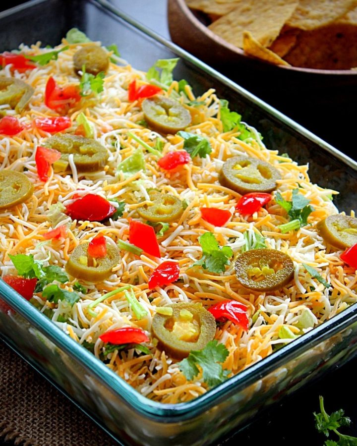 7 layer bean dip served in a glass tray garnished with jalapeno, tomato and coriander and served with tortilla chips and salsa