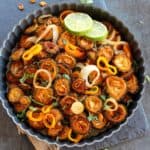 Baked sweet and sour karela served in a pan garnished with cilantro and some lime slices