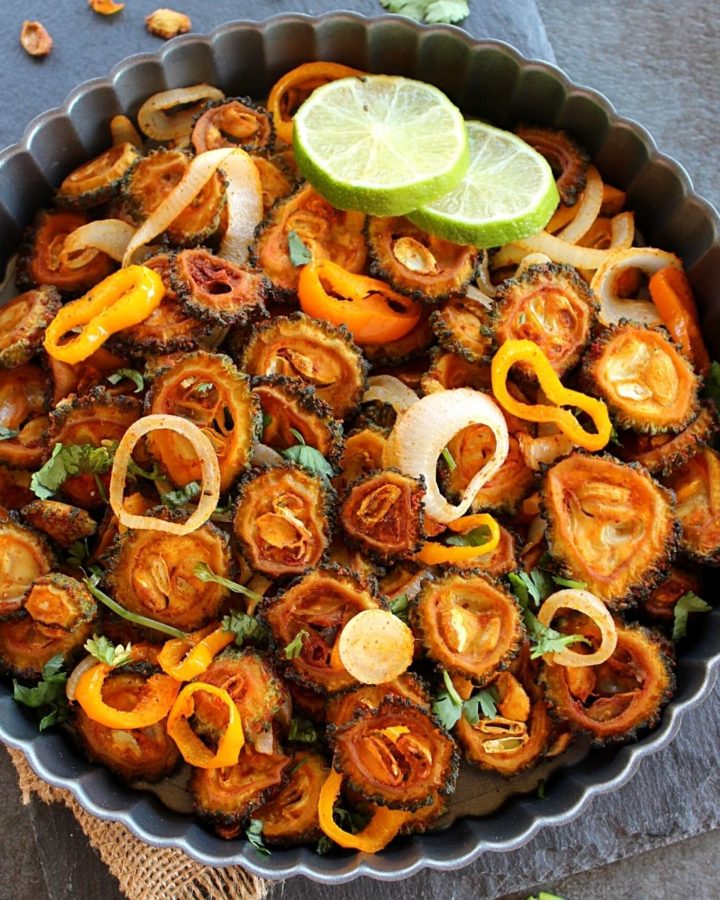Baked sweet and sour karela served in a pan garnished with cilantro and some lime slices