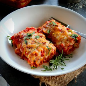2 veggie lasagna rolls ups served in a white plate garnished with fresh herbs