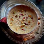 quinoa kheers served in a large silver bowl garnished with rose petals, saffron and nuts