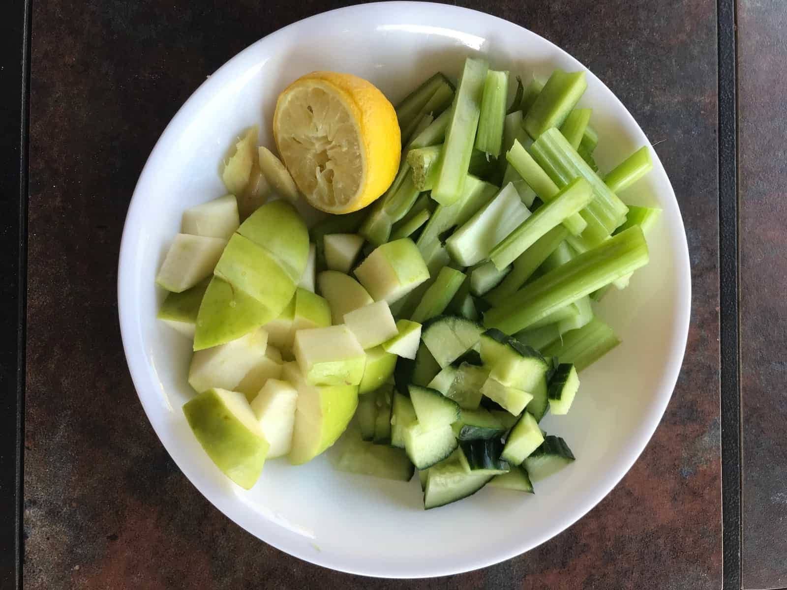 celery, cuucmber, apple, ginger and lemon arranged in a white plate