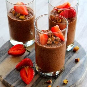 chocolate chia pudding served in three glass cups topped with pistachio and strawberry