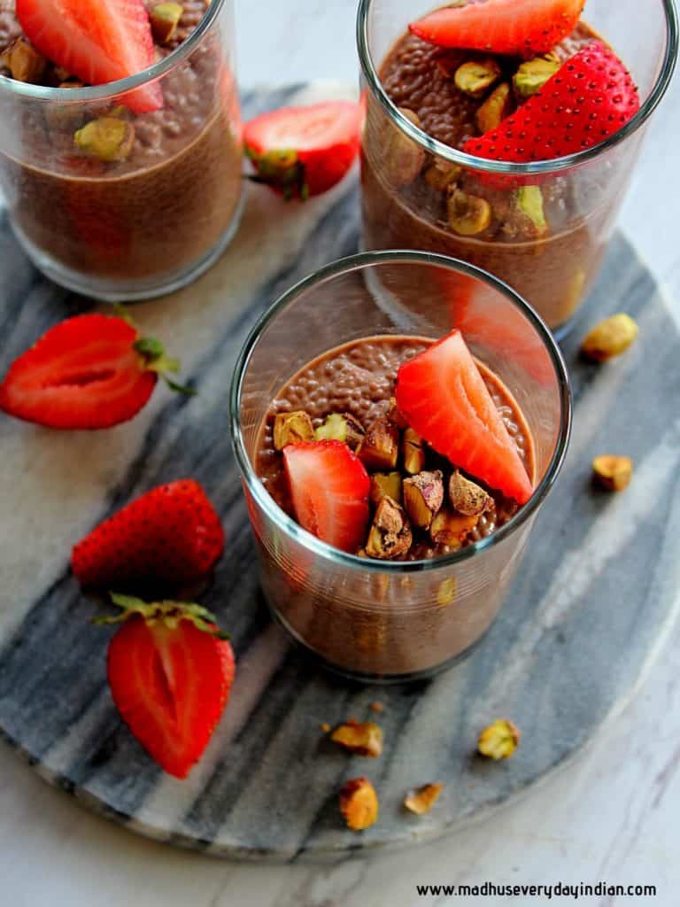chocolate chia pudding served in three glass cups topped with pistachio and strawberry