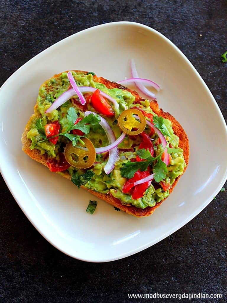 guacamole toast topped with red onion, jalapeno, tomato and cilantro on a crusty bread