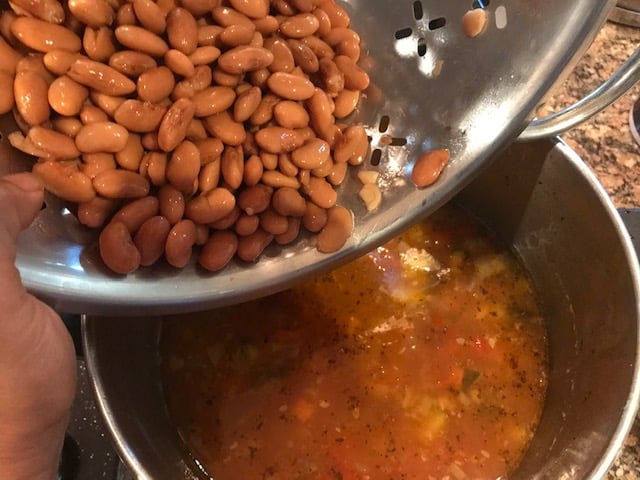 pinto beans being added to the vegetable soup