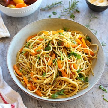 spaghetti with garlic and olive oil served in a large plate garnished with parsley and on the side are parmesan cheese and cherry tomato