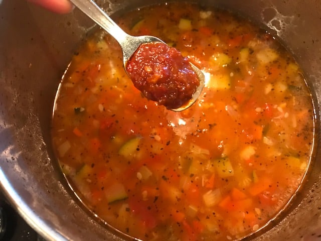 hot chili garlic sauce being added to the vegetable pinto beans soup