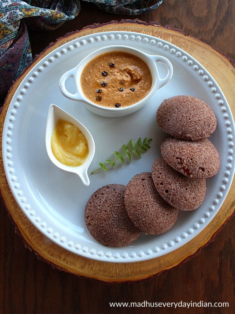 5 ragi idli served in a white plate with ghee and peanut chutney