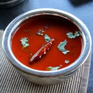 tomato paste rasam served in a steel bowl garnished red chili and coriander leaves.