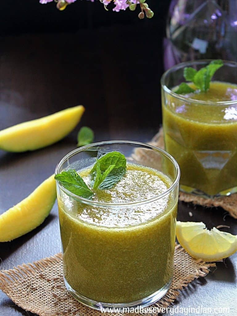 aam panna with out boiling served in a glass cup garmished with mint and lemon and mango slices on the side.