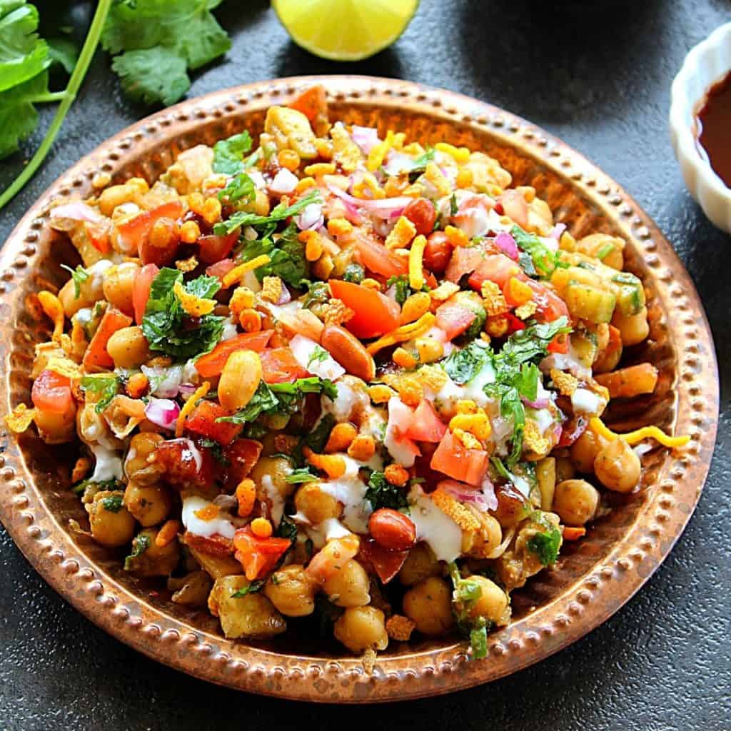 chana chaat served in copper plate served with coriander leaves and lemon slices.