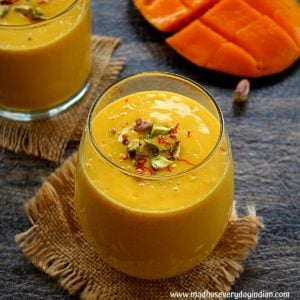 mango lassi served in a glass cup garnished with crushed pistachio and saffron.