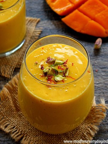 mango lassi served in a glass cup garnished with crushed pistachio and saffron.