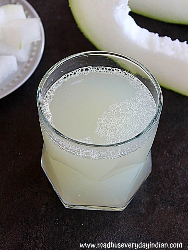 ash gourd juice served in a glass cup and in the back ground is a piece of ash gourd and few ash gourd pieces