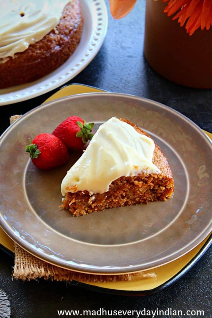 slice of carrot cake with velvety cream cheese frosting served with 2 strawberry