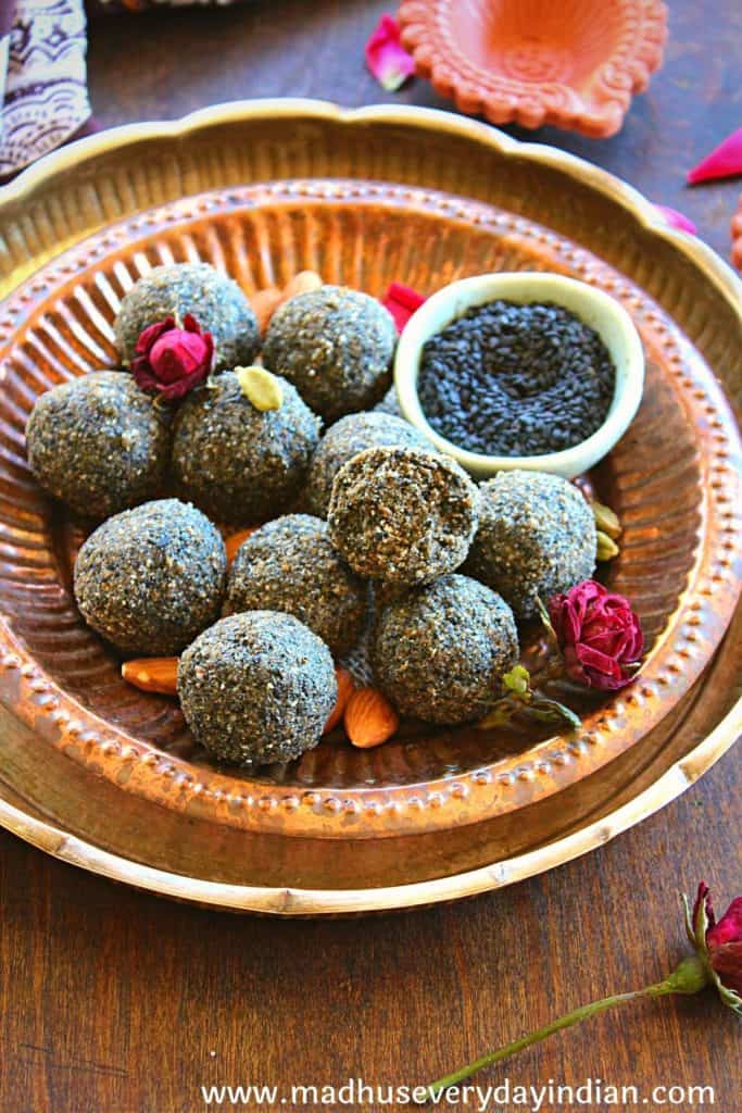 black sesame ladoo arranged in a copper plate garnished with almonds, cardamom and roses