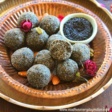 black sesame ladoo arranged in a copper plate garnished with almonds, cardamom and roses