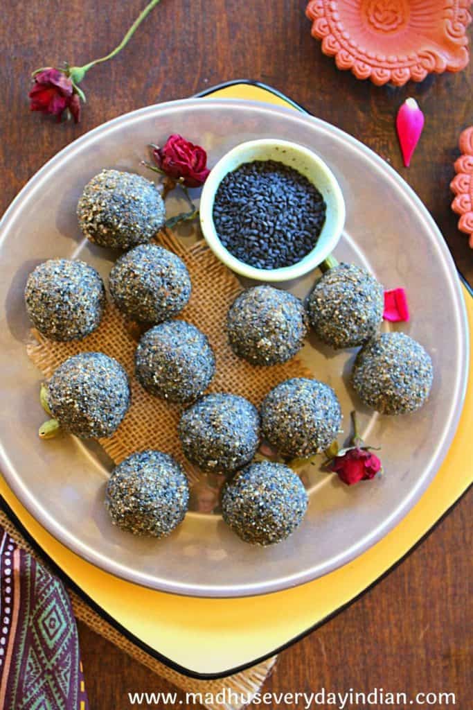 12 black sesame ladoo arranged in a yellow plate with cardamom and roses