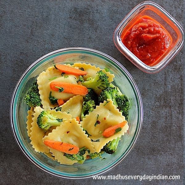 ravioli and veggies served in a glass container and marinara sauce