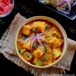 paneer curry served in a yellow bowl garnished with sliced red oniona nd coriander leaves