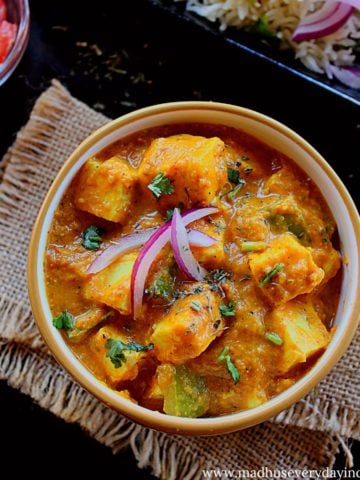 paneer curry served in a yellow bowl garnished with sliced red oniona nd coriander leaves