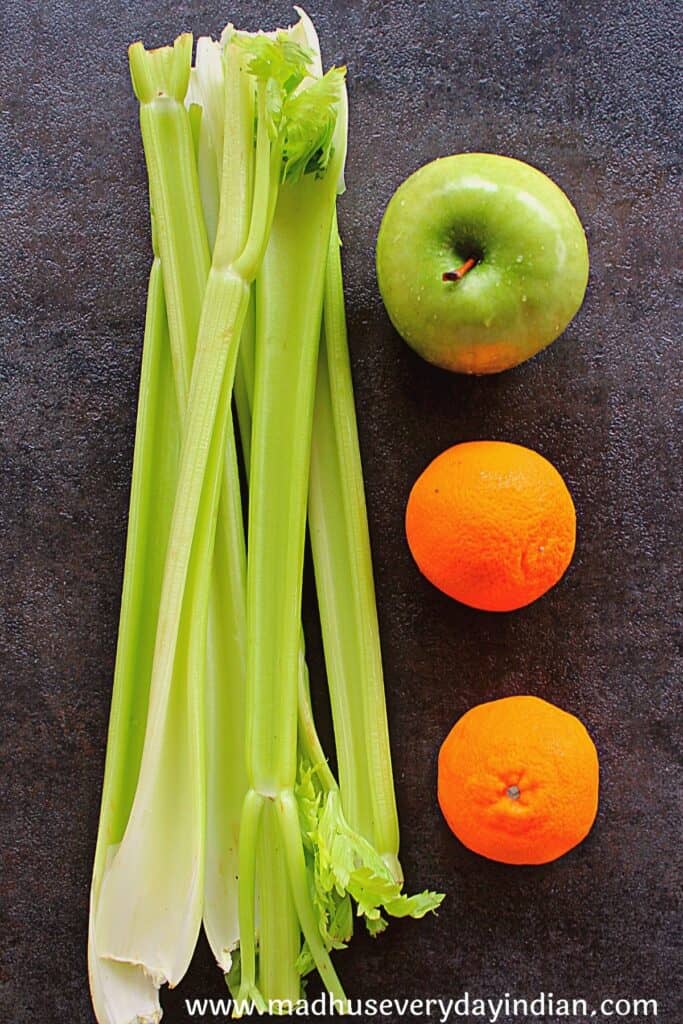 celery stalks, green apple and 2 mandarin oranges on a black board