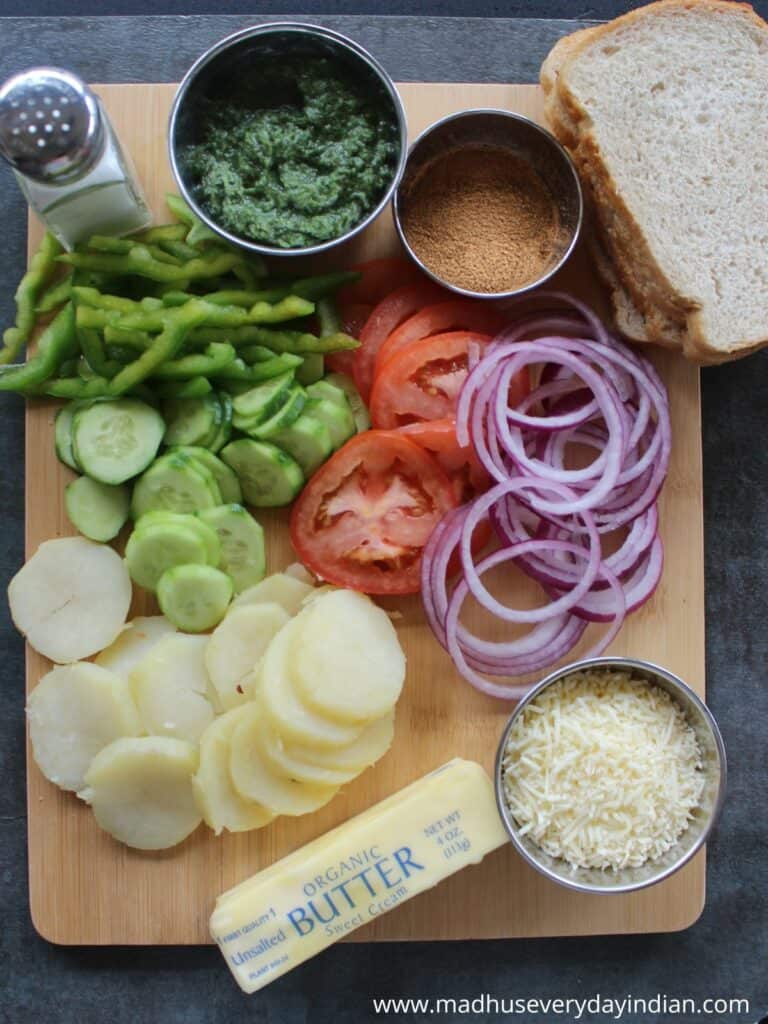 differnet veggies, sour dough bread , butter and cheese arranged in a wooden board for making mumbai sandwiches