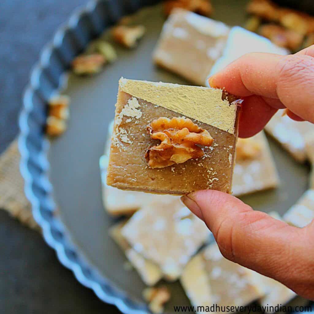 a piece of walnut burfi is held with your fingers 