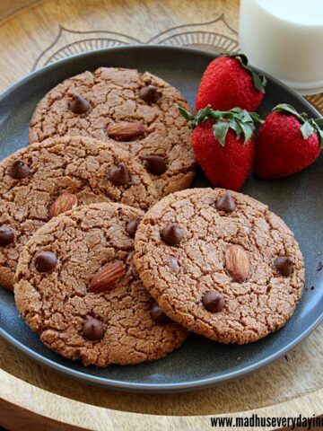 4 chocolate almond cookies placed in plate with strawberries and milk
